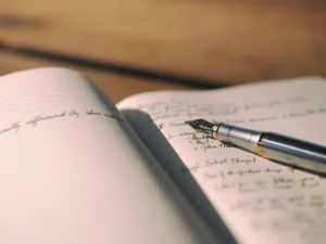 ノートの上に万年筆が置かれ、手書きのメモが書かれている様子